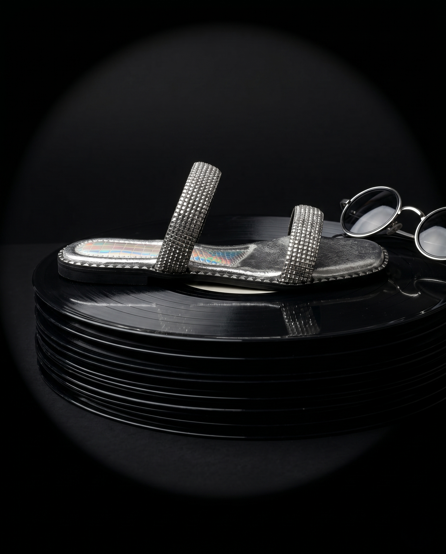 Crystalline Silver Flats on stacked vinyl records by Solemates by Palak — silver crystal double strap flat sandal with holographic lining and silver stud trim, dark studio backdrop