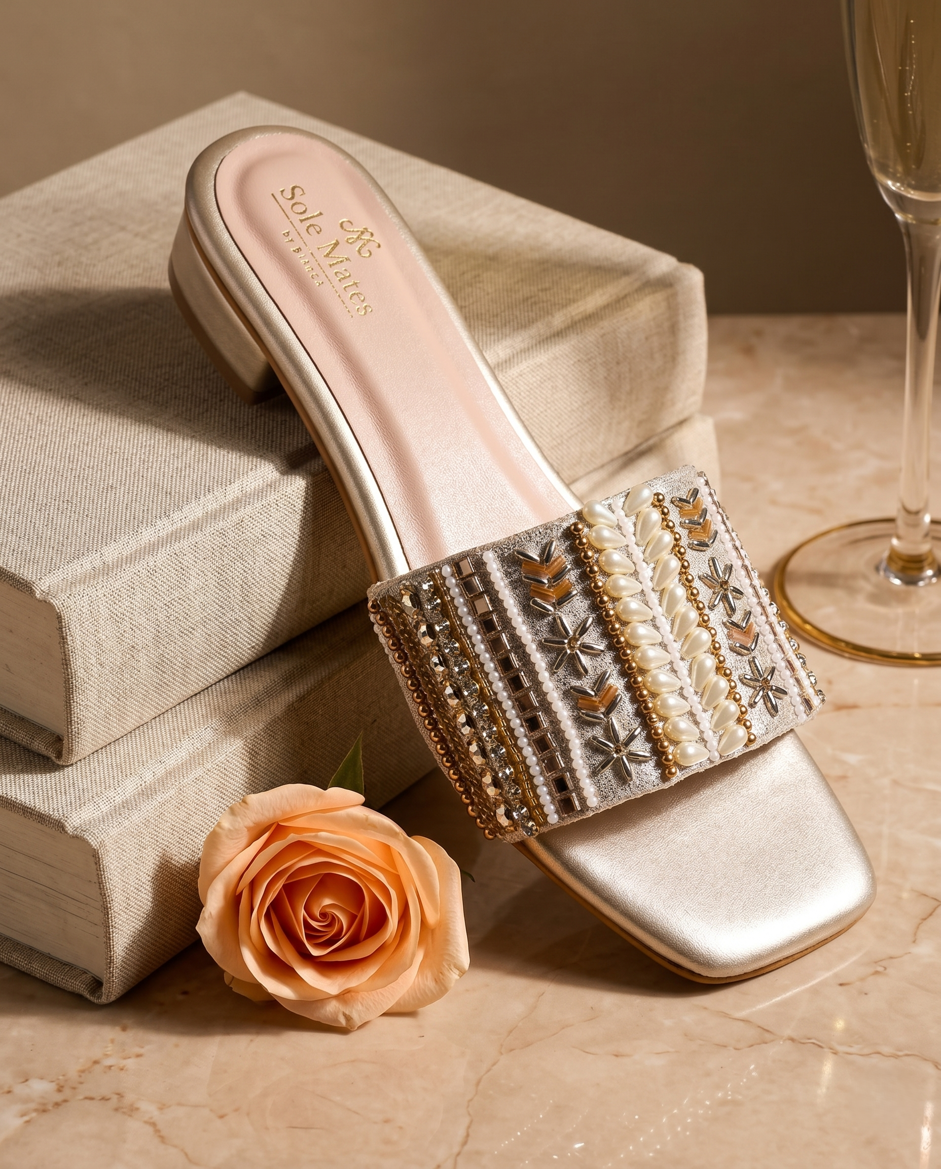 Kate Gold Sliders against linen books with peach rose and champagne flute — champagne gold embellished bridal sliders by Solemates by Palak