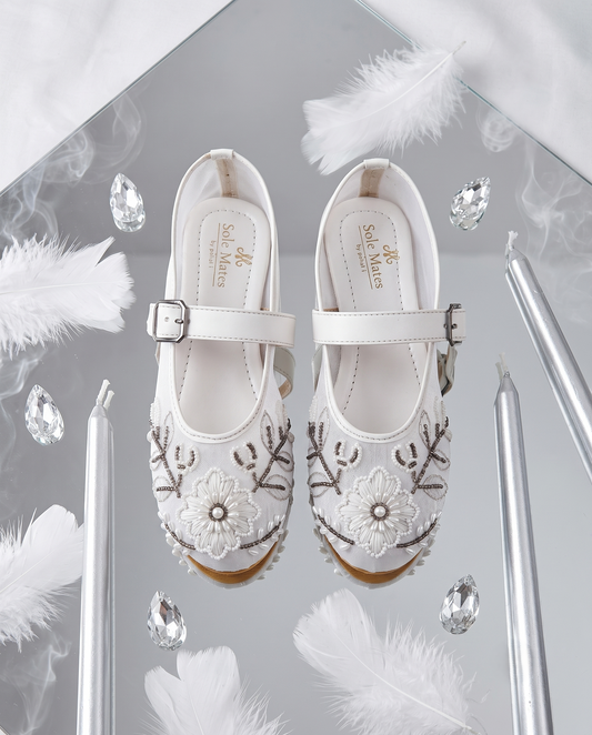 The Ballet Bloom Mary Janes flat lay on mirror with feathers and crystals — white pearl and bead embellished floral shimmer Mary Jane ballerinas by Solemates by Palak